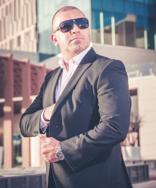 Agente de seguridad privada con traje negro y gafas oscuras, preparado para servicio de escolta y protección ejecutiva en un entorno urbano